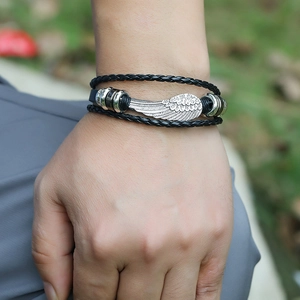 Braided black leather wrap bracelet with silver feather metal charm on a wrist