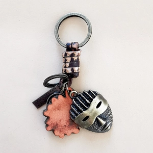 Detail of vintage woven leather keychain with bronze ring, masks and heart charm