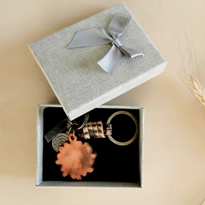 Detailed view of an orange flower leather keychain in a gray gift box with a metal charm