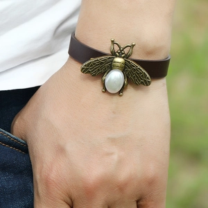Retro brown leather bracelet with bronze bee and pearl on a person's wrist outdoors