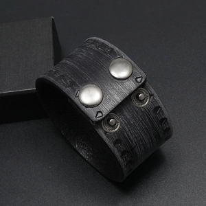 Macro shot of punk wide leather bracelet showing black wood-grain texture and metal snaps