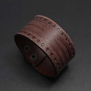 Close-up of wide vintage brown leather bracelet with embossed patterns and metal snaps