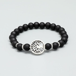 Matte black beaded Tree of Life bracelet with silver charms on a grey background