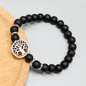 Matte black beaded tree of life charm bracelet on a minimalist wooden tray display