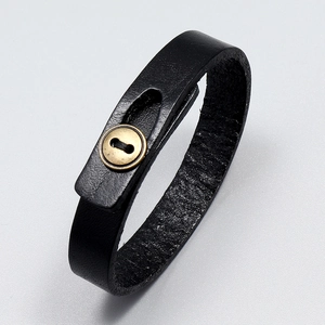 Close-up of black leather bracelet with a brass button clasp on a grey background
