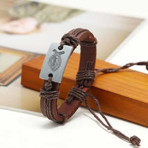 Detail of woven brown leather bracelet with rectangular metal plate on wooden base