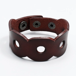 Detail view of brown wide leather bracelet featuring hollow circles and bronze snap buttons