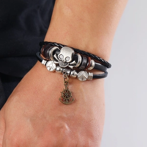 Detail of multi-layer leather bracelet with silver skull and anchor charms on wrist