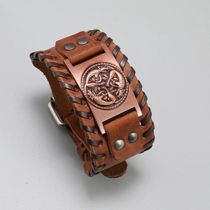 Detail of vintage brown leather cuff featuring Celtic wolf knot metal charm and braided edges