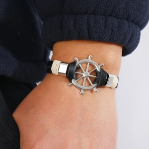 Nautical black leather bracelet with silver ship wheel charm worn on the wrist