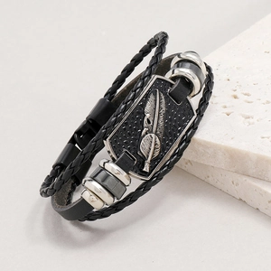 Dettaglio del bracciale in pelle multistrato con ciondolo a piuma d'argento su marmo