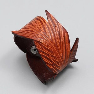 Macro detail of brown leather bracelet featuring intricate feather embossing and silver snap