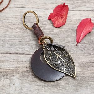 Vintage leather keychain with antique bronze leaf pendant on rustic wooden background