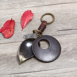 Vintage woven leather keychain with bronze leaf pendant on light wood background