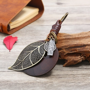 Vintage braided leather keychain with bronze leaf pendant and metal tag on wooden desk