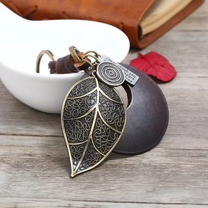 Vintage woven leather keychain with bronze leaf pendant and wood ring on a light wood surface