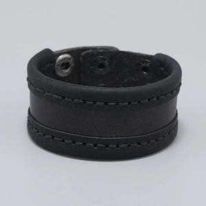 Detail of black leather cuff bracelet with hand-stitched edges and metal snap closure
