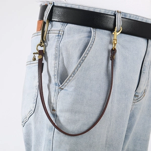 Retro leather waist chain with brass carabiner and bell charm on blue denim jeans
