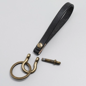Detail showing black lychee grain leather strap with brass horseshoe D-ring and key ring