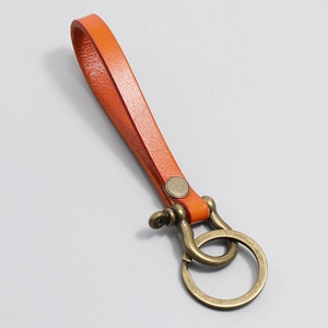 Close-up of bright orange vintage leather keychain with antique bronze D-ring and rivet