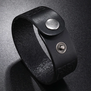 Macro detail of black leather cuff featuring embossed vintage totem patterns and snap button