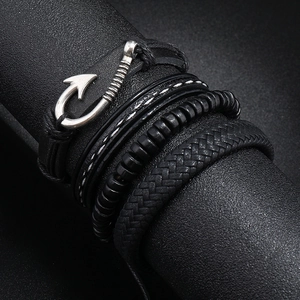 Macro detail of men's multilayer black leather bracelets with silver fishhook charm and braid
