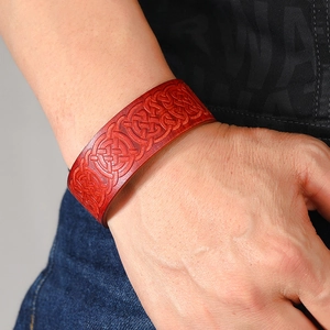 Red leather cuff bracelet with Celtic knot embossing worn on a denim background