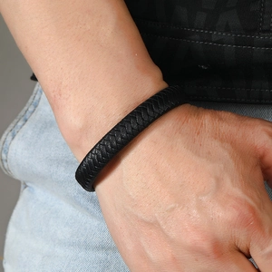 Close-up of black braided leather bracelet with fishbone weave pattern and metal clasp