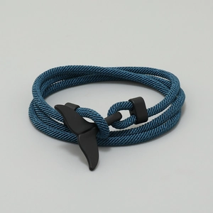 Macro detail of teal ocean-themed woven cord bracelet with matte black whale tail clasp
