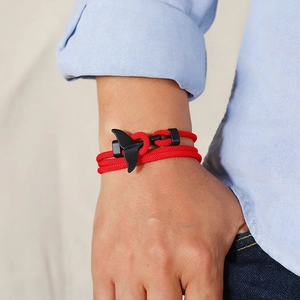 Detail of red braided ocean style bracelet with a matte black whale tail metal clasp