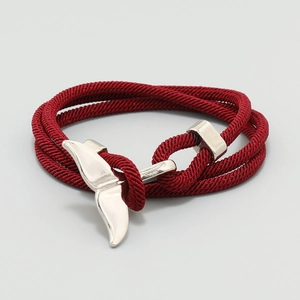 Detailed view of red nautical braided cord bracelet with silver whale tail charm