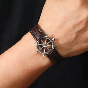 Detail of nautical leather bracelet featuring a silver steering wheel anchor charm on wrist