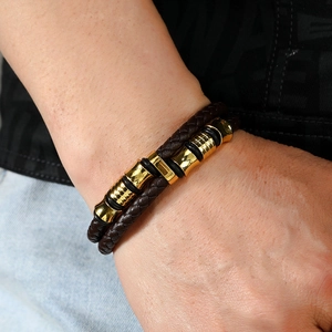 Gros plan d'un bracelet en cuir tressé marron pour homme avec cylindres en métal doré