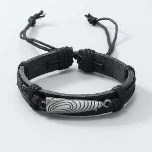 Close-up of woven leather bracelet featuring a spiral engraved silver metal charm