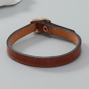 Detail eines braunen Lederarmbands mit goldenem Verschluss und Vintage-Niete