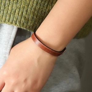 Minimalistisches braunes Lederarmband mit Metallschnalle am Handgelenk mit Strickpullover