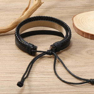 Dettaglio del bracciale in pelle nera intrecciata con cordino regolabile su legno