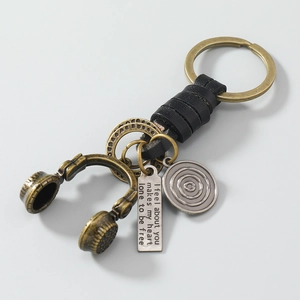 Detail of vintage bronze headphone charm and engraved pendant on woven leather keychain