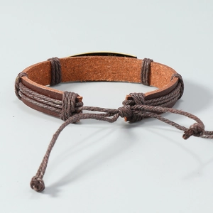 Detail of brown braided leather bracelet featuring vintage bronze etched metal plate
