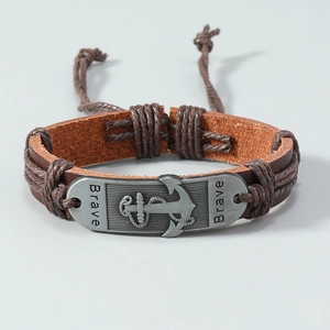 Macro detail of brown leather braided bracelet with a silver anchor plate and Brave engraving