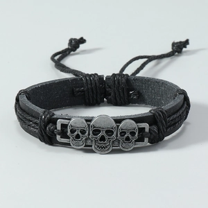 Detalle de pulsera de cuero trenzado negro con tres calaveras plateadas de estilo punk
