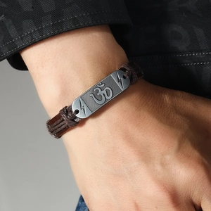 Detailopname van bruine gevlochten leren armband met gegraveerde Om-symbool metalen plaat