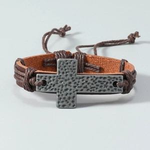 Close-up of vintage brown leather woven bracelet with silver cross and hammered texture