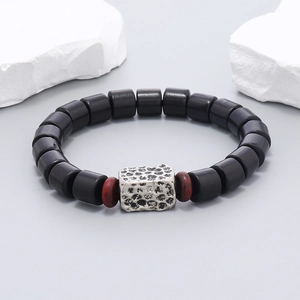 Detail of beaded bracelet with black wood beads and silver hammered square metal charm