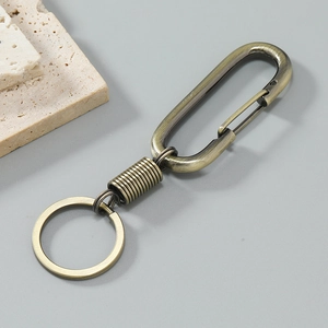 Retro bronze metal car keychain with spring link and carabiner clip on stone backdrop