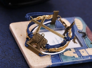 Détail de bracelet tressé avec croix en bronze, pendentif éléphant et barre courage