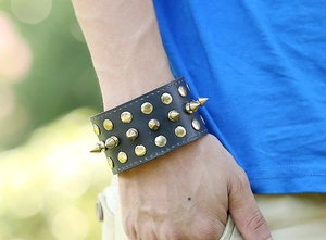 Detail of a punk rock wide black leather bracelet with gold conical spikes and round studs