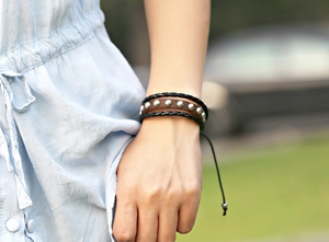 Close-up of a three-layer leather rivet bracelet with adjustable braided cords on a wrist
