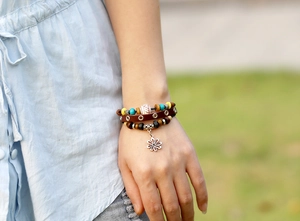Detail eines mehrlagigen Lederarmbands mit Perlen und Metall-Blumenanhänger am Handgelenk