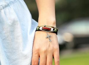 Détail d'un bracelet en cuir multicouche avec pendentif croix argentée vintage